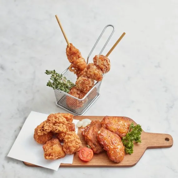 A platter of Japanese fried chicken featuring crispy Chicken Karaage, Tatsutaage, and glazed Chicken Wings served with a side garnish on a wooden board.