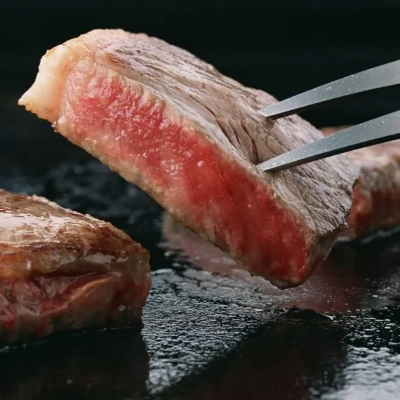 Searing a thick, succulent cut of premium Miyazaki Wagyu beef steak on a hot teppan grill, showing a perfectly browned crust and a juicy, tender pink center.