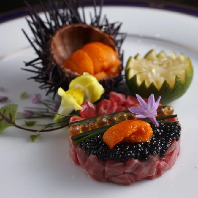 An exquisite Miyazaki Wagyu beef tartare topped with premium black caviar and fresh sea urchin (uni), beautifully presented with edible flowers and citrus.