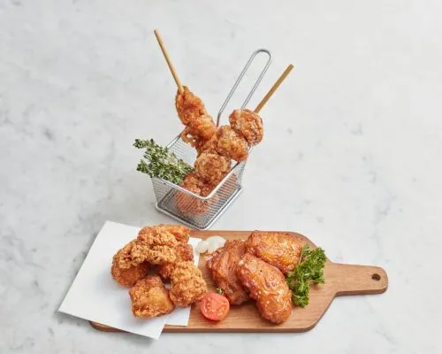 A platter of Japanese fried chicken featuring crispy Chicken Karaage, Tatsutaage, and glazed Chicken Wings served with a side garnish on a wooden board.